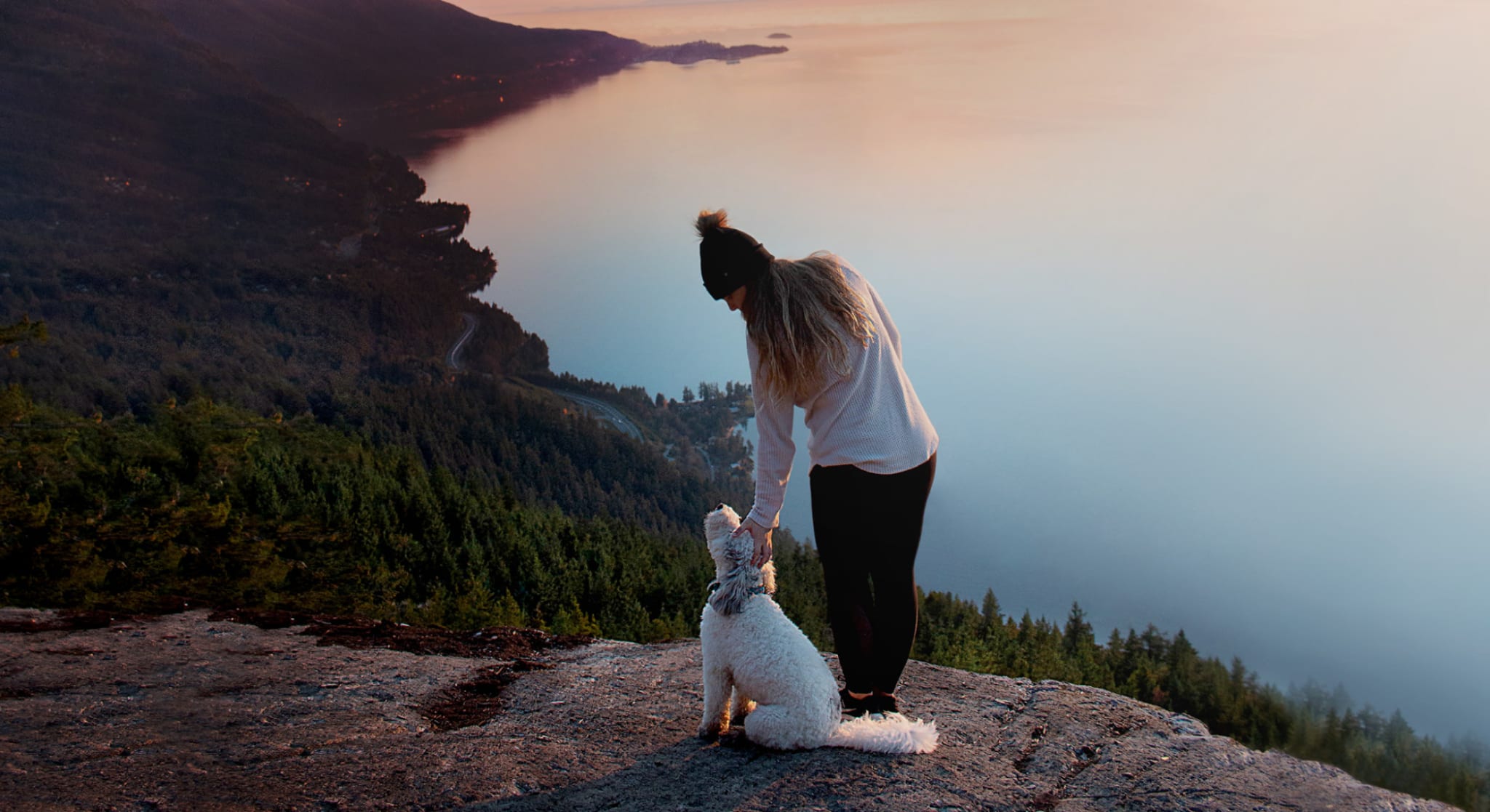 Woman petting dog on mountain overlooking lake and forest